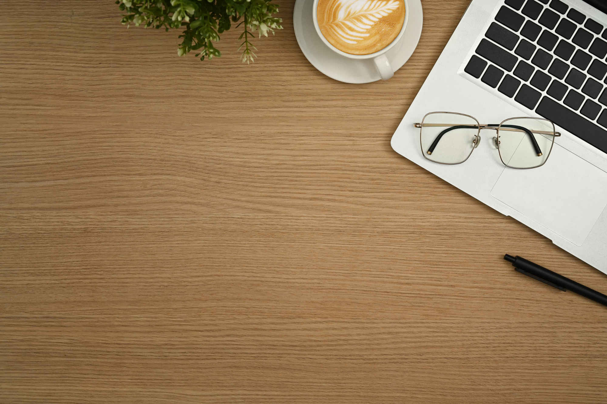 Laptop, glasses, and cup of coffee resting on a light colored wooden desk