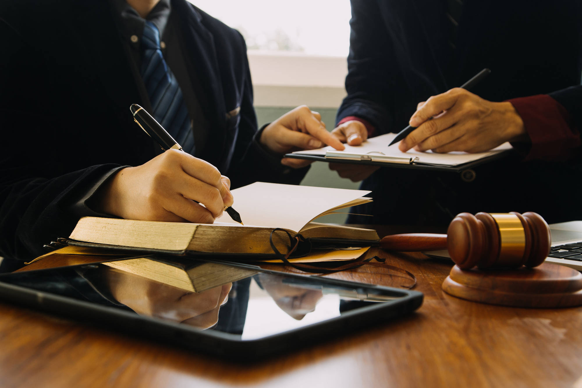 Two lawyers reviewing documents at a wooden desk with a gavel and a tablet device